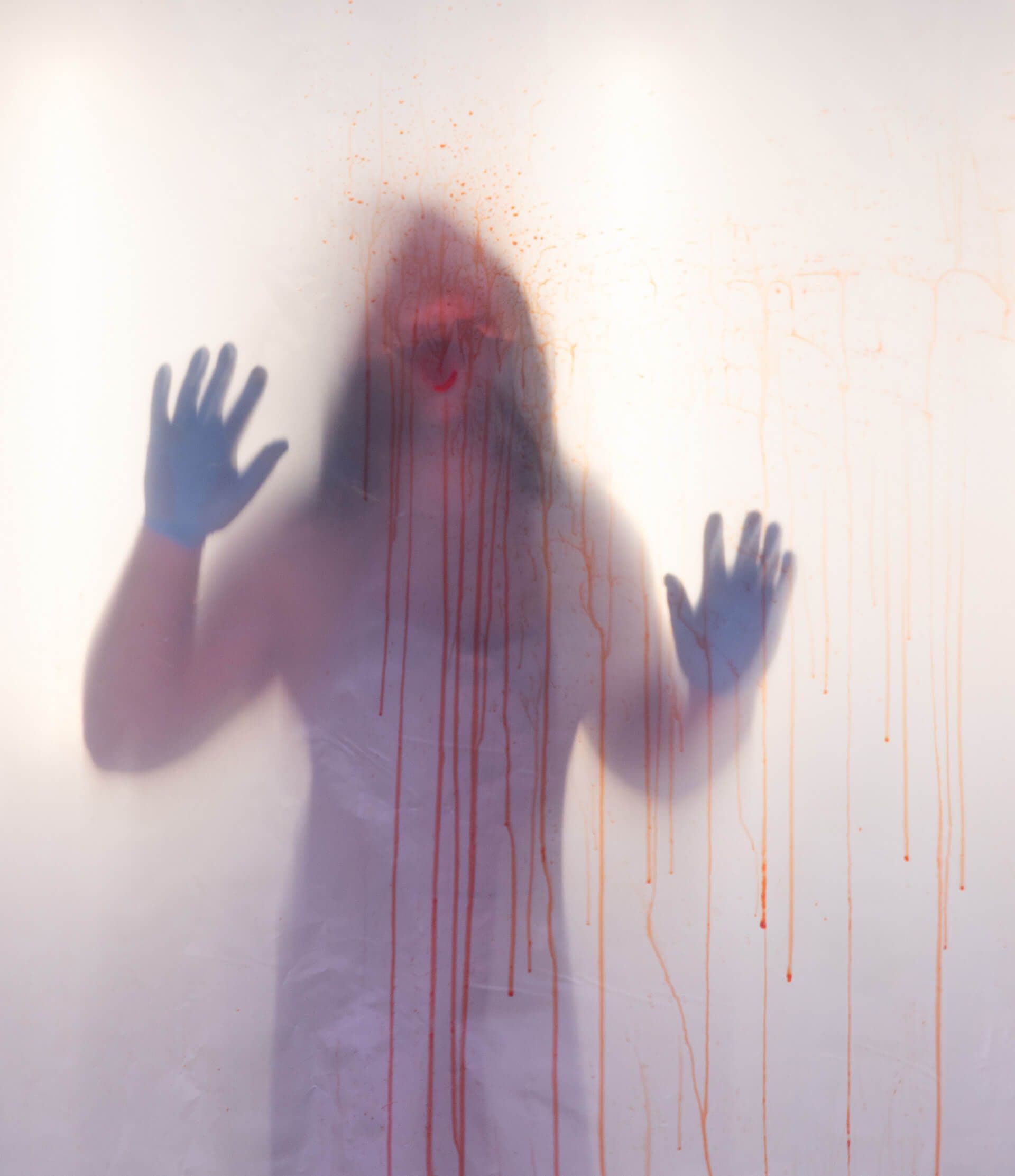 Image of a man leaning towards camera against a misty, bloody window